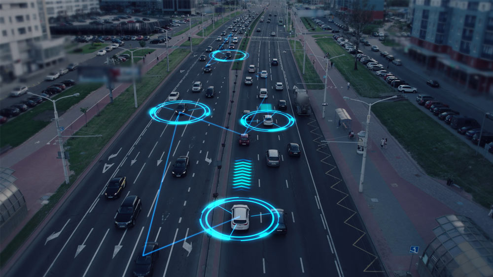 Die Grafik zeigt eine Luftaufnahme einer vielbefahrenen mehrspurigen Straße in einer Stadt. Autos sind auf den Fahrspuren unterwegs, während leuchtende blaue Linien und Kreise um einige Fahrzeuge herum Projektionen darstellen, die auf die Verwendung von Technologien für autonomes Fahren hinweisen.